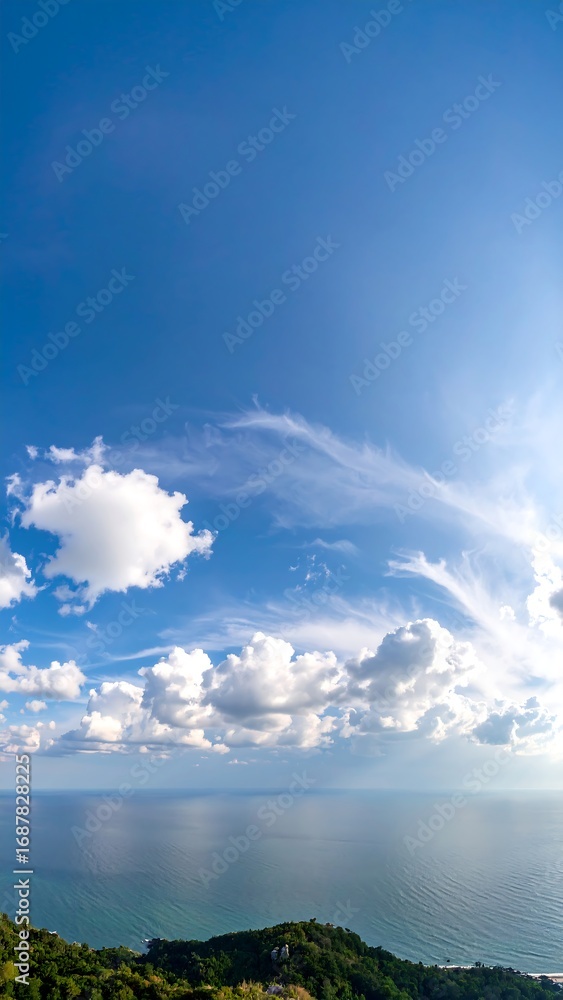 Obraz premium Panoramic view of a bright blue sky with puffy white clouds over a tranquil ocean and distant green hills