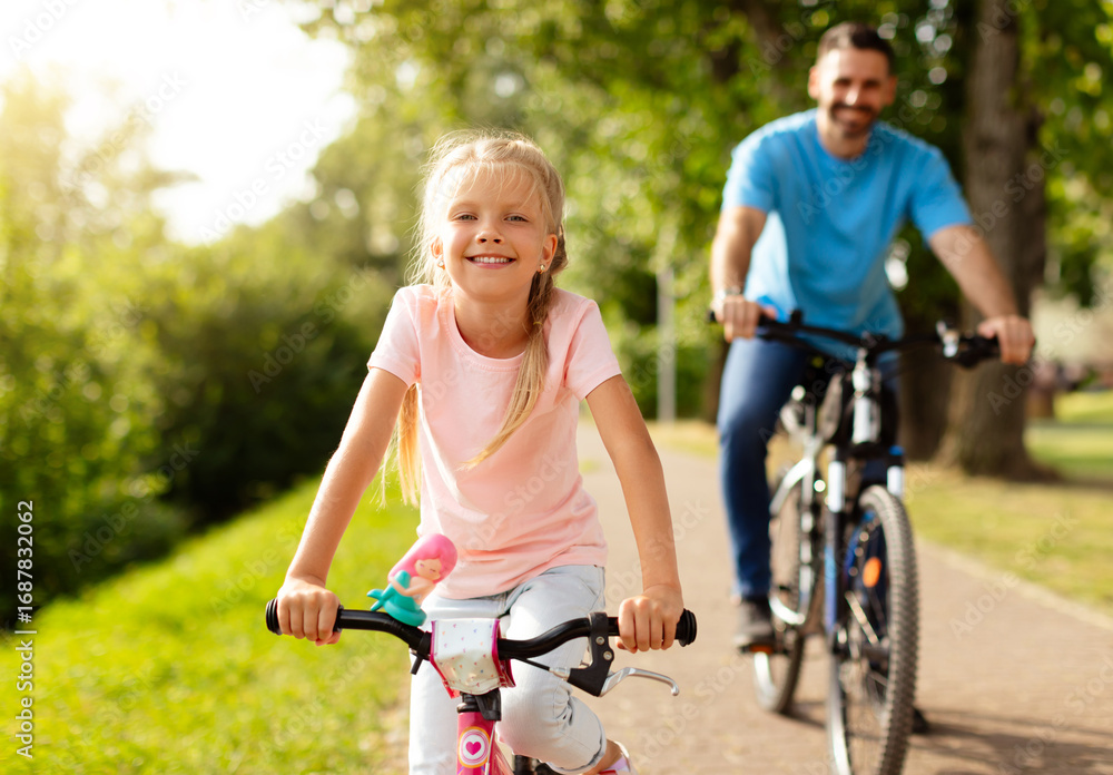 Obraz premium Day in the park. Happy family of caucasian father and girl child riding bicycles outdoors in the summer, smiling at camera. Dad and daughter's park adventure