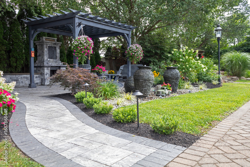 Wooden gray pergola on pavers with stone fireplace and waterfall urns landscape design idea for backyard sanctuary