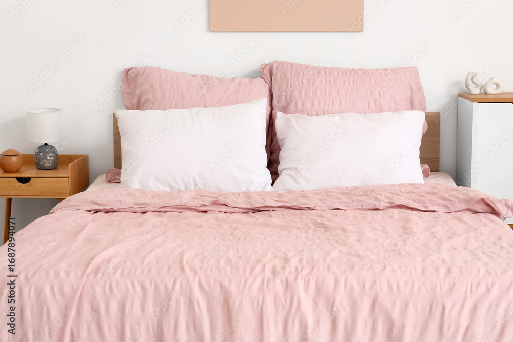 Obraz premium Bed with stylish pink bedding and bedside table in bedroom