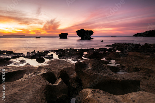 Coastal rock formations silhouetted against a vibrant sunset over the ocean at Coffin Bay, South Australia.