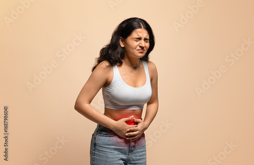 Φωτογραφία Sick young indian woman having stomach ache, touching her abdomen with red infla