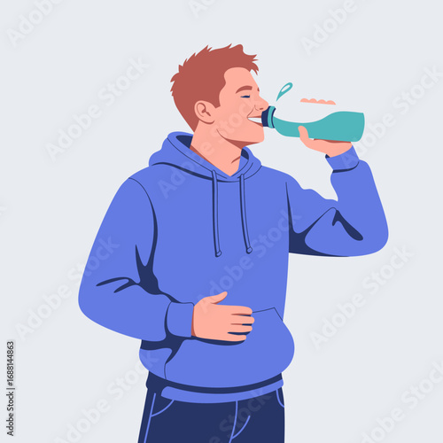 A cheerful young man enjoying a sip from a water bottle while wearing a blue hoodie, showcasing a refreshing moment filled with joy and energy in a stylish pose.