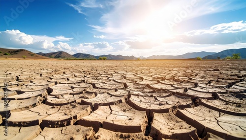 Cracked dry earth under a blue sky with clouds and distant mountains