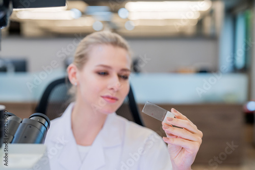 Free Download Scientist examines slide under microscope in contemporary laboratory setting during daytime - GFXLoad