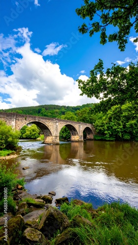 Wallpaper Mural A stone arch bridge over a calm river, framed by lush greenery and a vibrant sky Torontodigital.ca