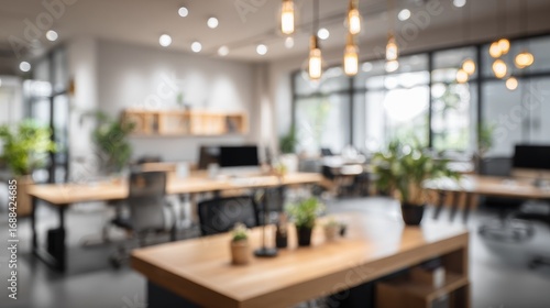 Blurry office scene featuring natural wood desks, potted plants, and overhead pendant lights. A modern, open work environment
