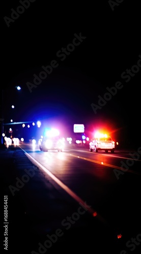 Blurred image of police vehicles on a dark highway at night. Flashing red and blue lights illuminate the scene, creating a sense of urgency
