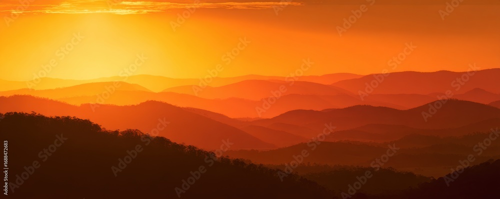 Fototapeta premium Golden sunset over a range of mountains. Silhouette of forested hills bathed in warm, orange light