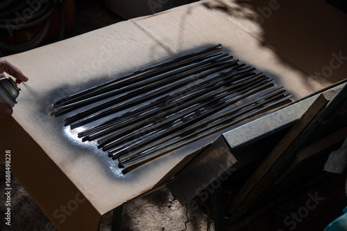 Φωτογραφία Hand spray painting a set of black metal rods on cardboard surface in sunlight,