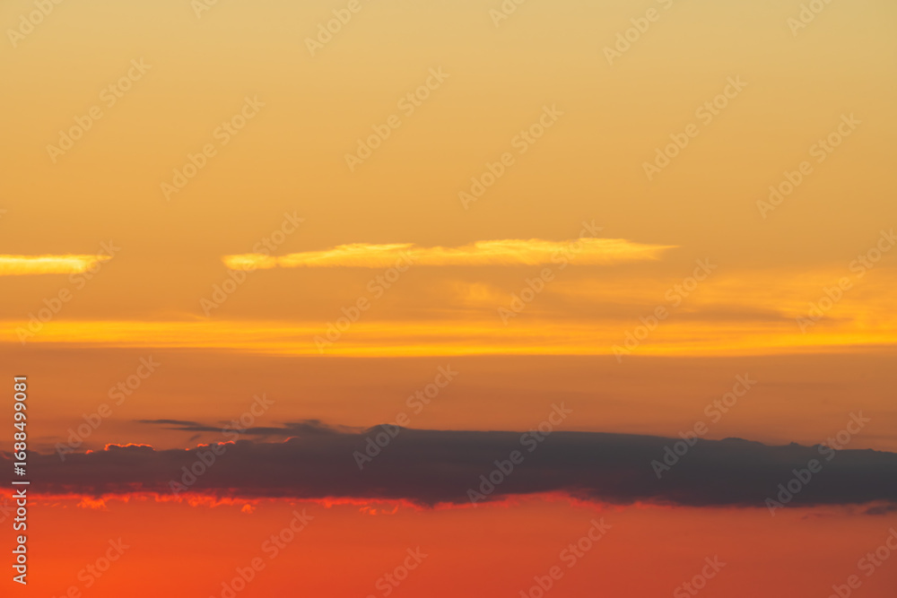 Obraz premium Vibrant colorful sunset sky with a warm orange and red gradient, featuring layers of dark and glowing clouds.