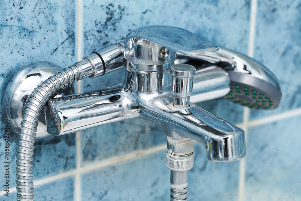 Obraz premium Bathroom chrome faucet with shower hose. Water tap closeup on blue tiles background. Sanitary installation in home interior. Plumbing equipment detail. Household bathroom hygiene element.