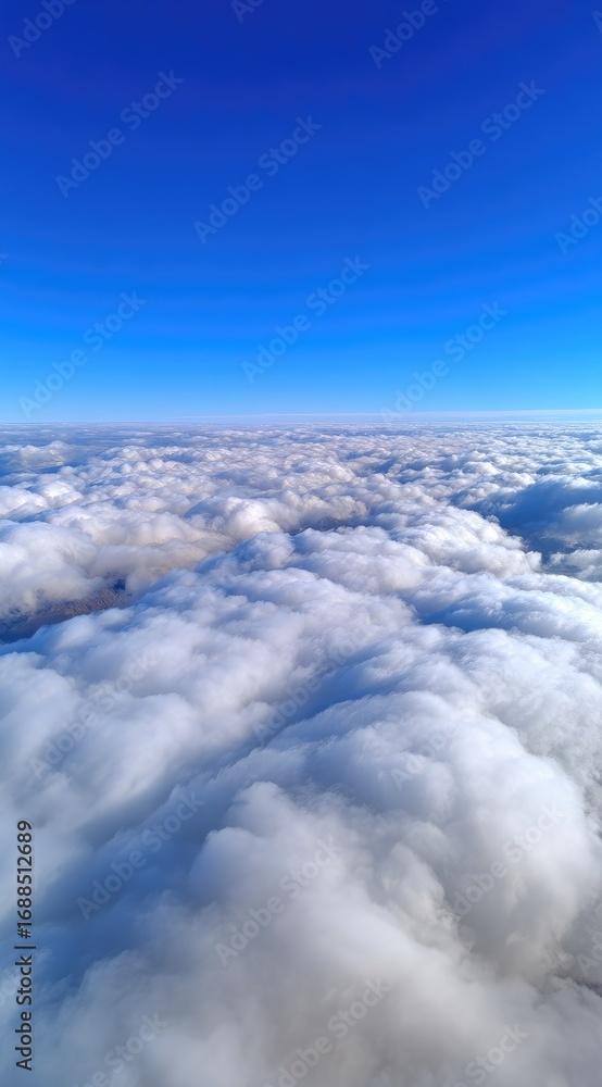 Naklejka premium A high-angle view presents a sea of fluffy white clouds under a clear, vibrant blue sky. Suggestive of flight or looking down from a great height