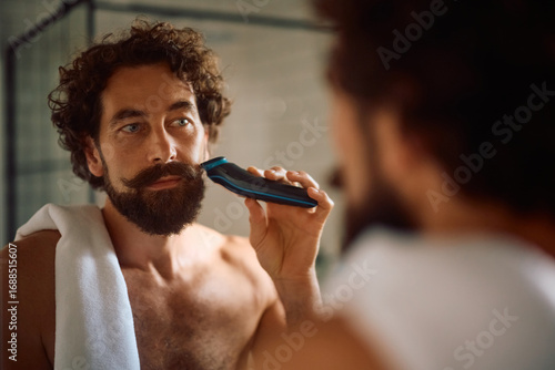 Bild auf Leinwand Mature man using electric razor while shaving in bathroom.