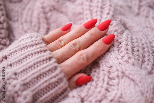 Red manicure against the background of a knitted pink sweater. Beautiful long oval nails.