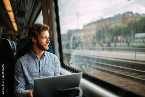 Young professional sitting in a moving train or bus, working on laptop, city view through window