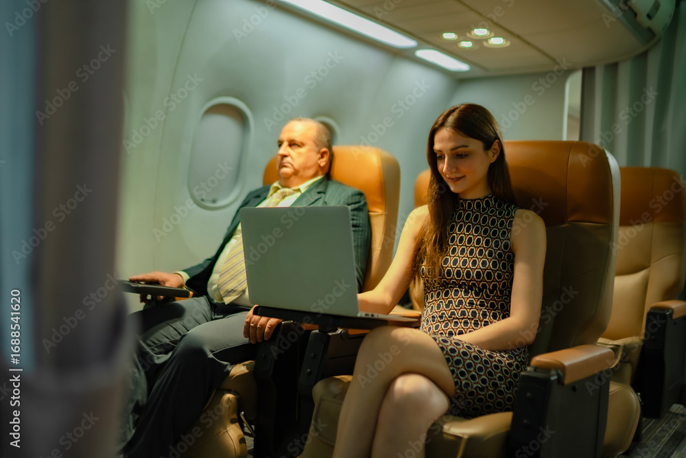 Fototapeta premium Smiling overweight businessman seated next to woman working on computer during flight. Idea of inflight productivity, business trip, technology use, airline service, and international travel industry.