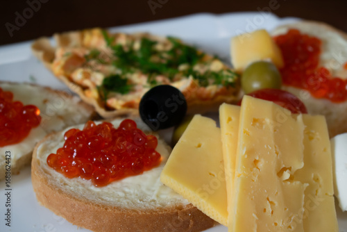 Sandwiches with red caviar, cheese and olives on a plate close-up