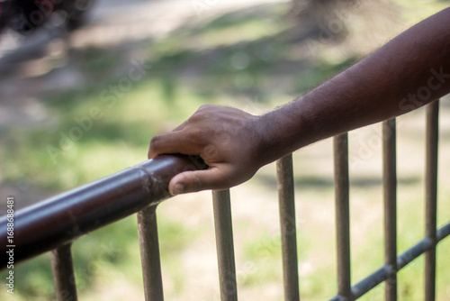 A persons hand rests on a metal railing outdoors