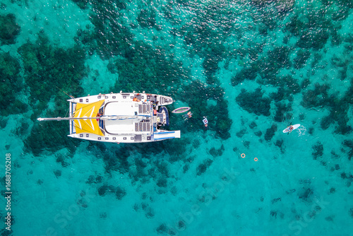 Aerial top view of sailing catamaran anchor over turquoise water with tourists swimming and paddle boarding at Racha Yai Island, A popular destination for summer vacation in Phuket, Thailand.