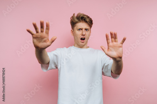 portrait of young dismayed man raises his hands in shock and disbelief, capturing an intense emotional moment on pink background
