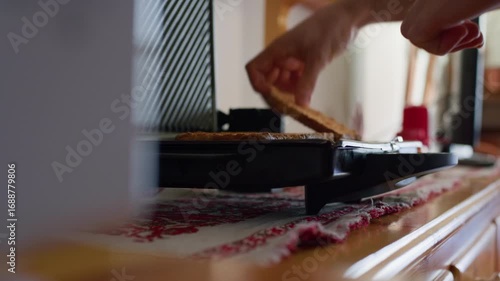 Hand removes toasted bread from a black toaster on a wooden counter, close-up, kitchen appliance in action.