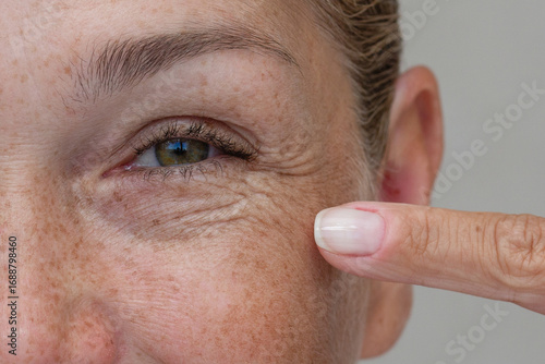 Close up cropped view of a middle aged woman laughing and pointing at crows feet with her finger