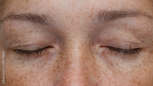 Close-up of closed eyes of a middle-aged woman with hooded eyelids and freckles