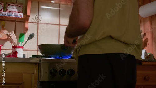 Tripod closeup of a pan on the stove with a man cooking in a wooden mountain cabin at night, highlighting food preparation details.