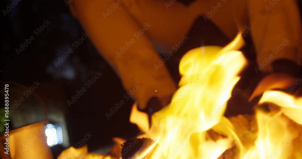 Fototapeta premium Crackling flames roaring around logs in outdoor fire pit, with boots and pants above