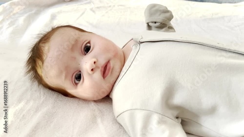 Little newborn baby lying on back smiling and looking at camera. Concept of healthy development of baby 0-6 months, baby care.