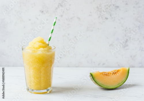 Melon slush drink in glass with green straw beside melon slice  