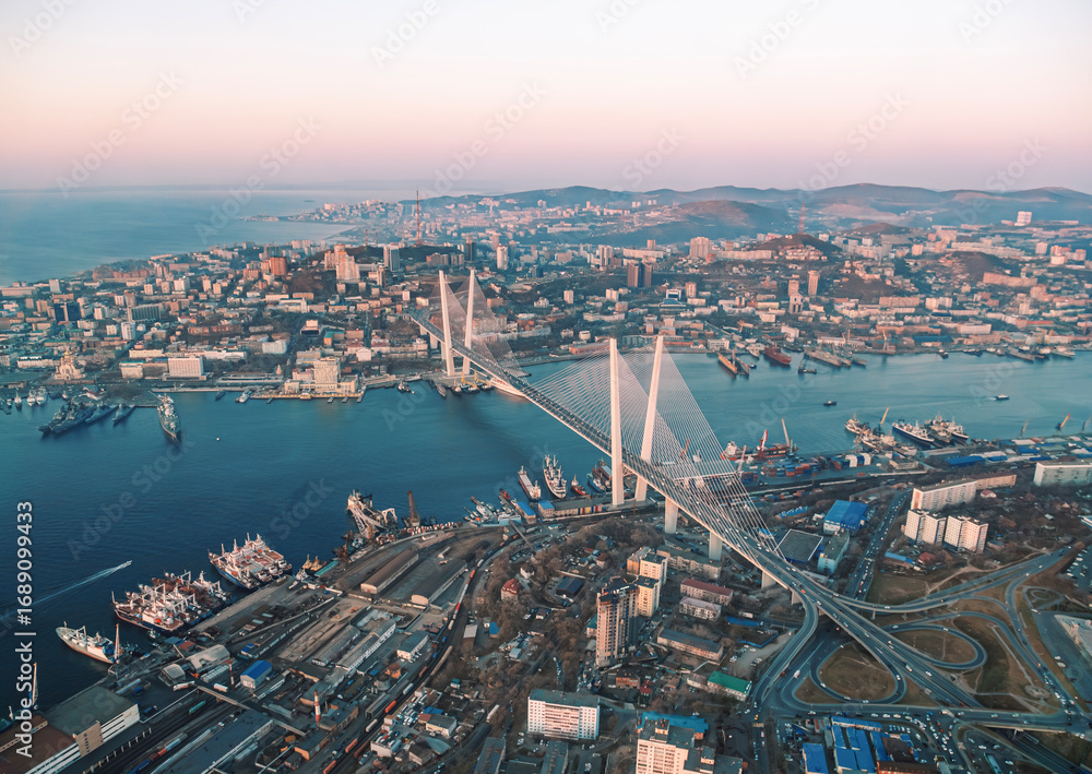 Obraz premium Aerial cityscape of Vladivostok at sunset showcasing urban development and the famous bridge connecting urban areas