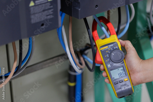 Hand Measuring Electrical Current with Yellow Clamp Meter