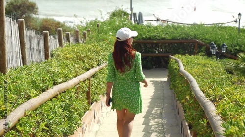 Beautiful Girl in Flowing Green Dress Descending Stone Steps Towards Ocean, Summer Travel Concept