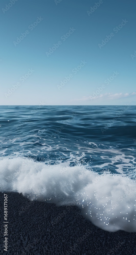 Fototapeta premium Ocean waves lapping at a dark pebble shore under a clear sky