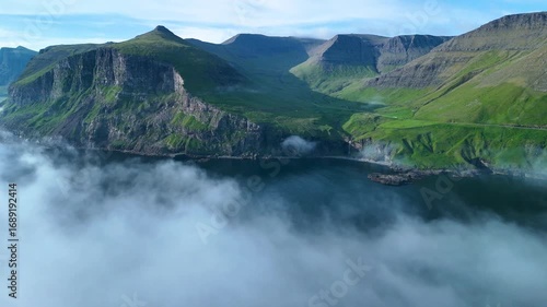 Explore the breathtaking cliffs and serene waters of the Faroe Islands, where dramatic rock formations rise above foggy shores, creating a captivating and tranquil atmosphere throughout the day.