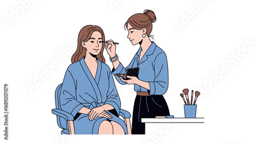 Professional makeup artist applying mascara to a seated woman in a blue robe with a brush holder nearby