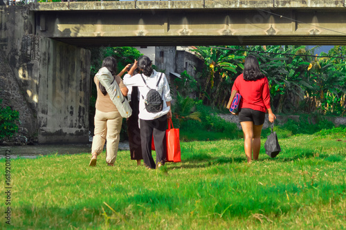 Wallpaper Mural A group of four girls walk together toward the bridge area, following the riverside path across the grassy meadow while carrying bags and supplies. Torontodigital.ca