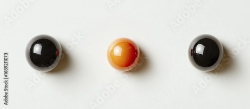 Minimalist composition of three glossy spheres: two black and one vibrant orb, arranged horizontally on a clean white background.