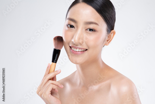 Asian Young woman holding makeup brush smiling with clean skin and natural beauty in studio session edit