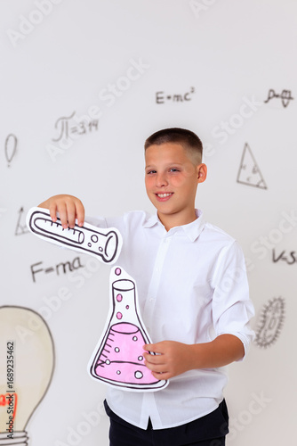 Thoughtful schoolboy in uniform sitting on wooden stool, student portrait with science and math formulas on white background, education and learning concept