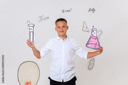 Thoughtful schoolboy in uniform sitting on wooden stool, student portrait with science and math formulas on white background, education and learning concept