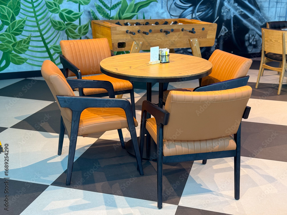 Fototapeta premium Round wooden table with leather chairs in a cafe interior near foosball game. Socialization, dining, and leisure illustrated as part of travel lifestyle and hospitality culture.