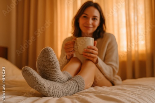 A woman relaxing in bed with a mug and knitted socks