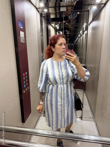 A woman in a striped dress takes a mirror selfie inside a modern elevator. Fashion, lifestyle, and self-portrait photography express individuality, identity, and everyday urban style.