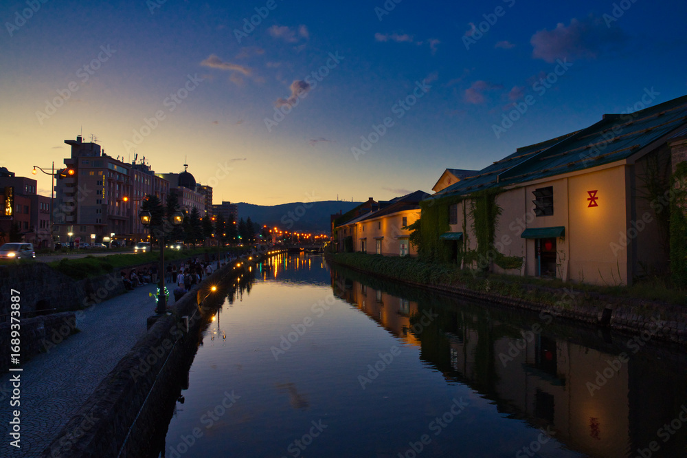 Naklejka premium 夕暮れ時の小樽運河、ノスタルジックな街並みと水面に映る灯り