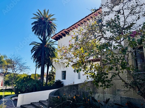 Exterior view of the Santa Barbara County Courthouse with palm trees, blooming flowers, and stone steps leading to the historic Spanish Colonial Revival building.