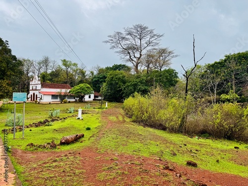 Wallpaper Mural A weathered cannon lies beside an old laterite fort wall, surrounded by green grass and red earth under a cloudy sky Torontodigital.ca