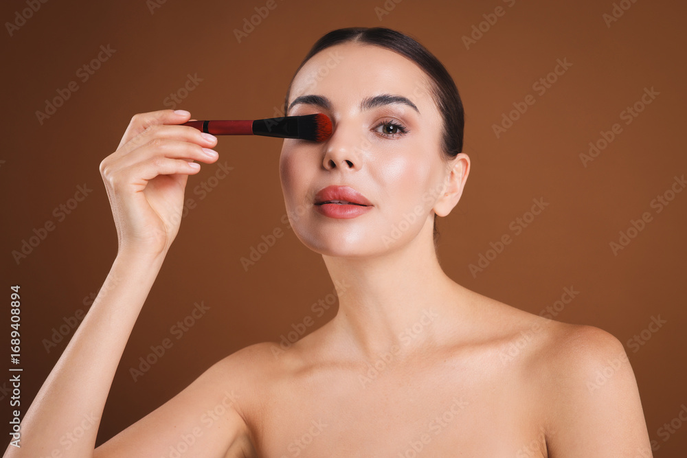 Obraz premium Beautiful woman with makeup brush on brown background
